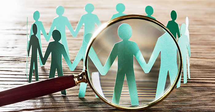 Eine Lupe zeigt auf einen Kreis von Papierfiguren, die sich an den Händen halten