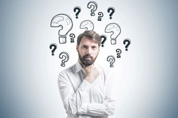 Ein Mann im weißen Hemd schaut fragend in die Kamera, um seinen Kopf herum sind viele Fragezeichen gemalt